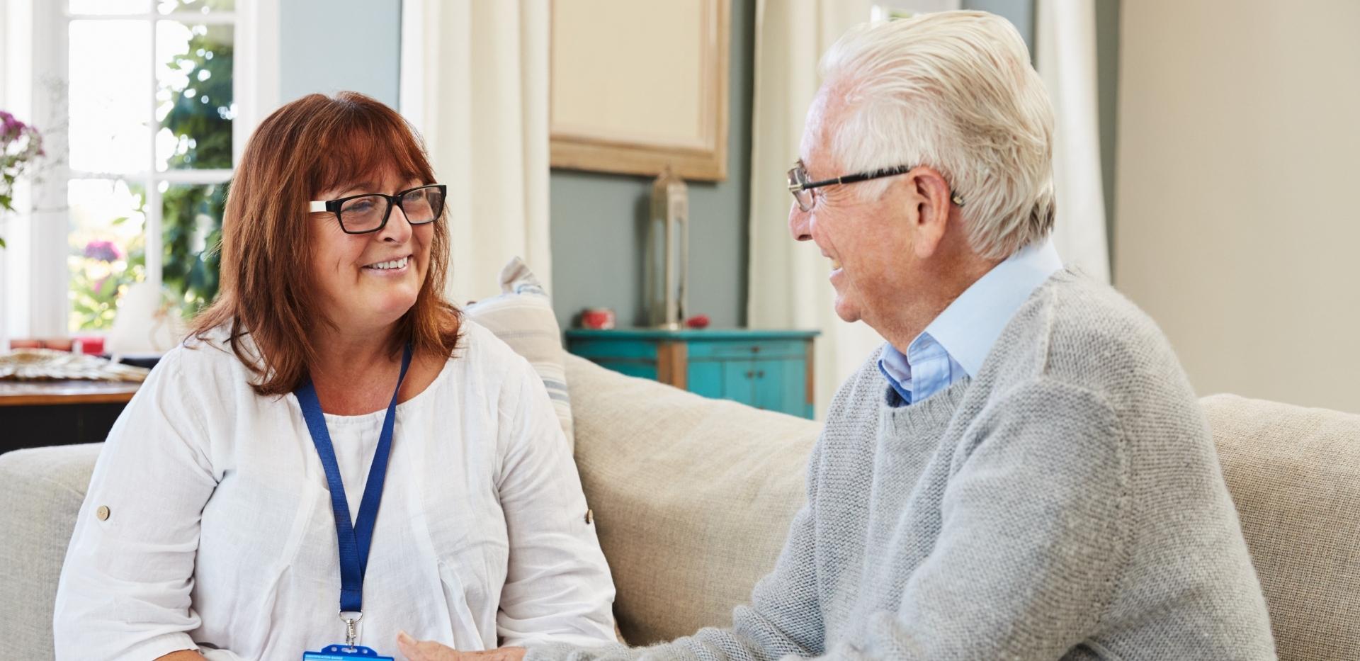 Female care worker smiling while talking with an older man on a couch